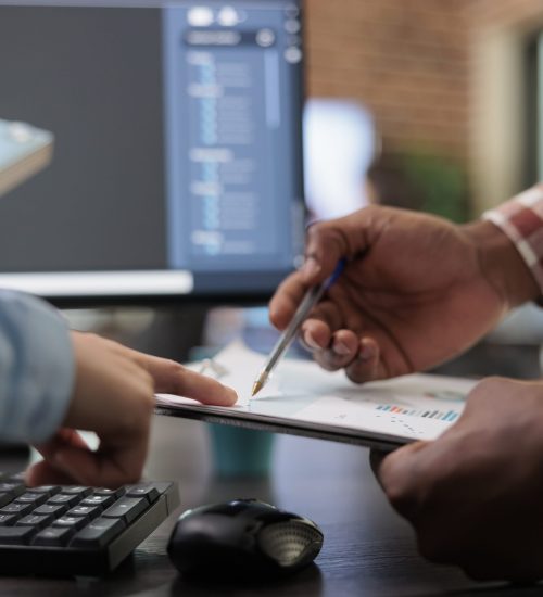 Close up of 3D digital artists reviewing sketch scene plan and simulated render times, Creative industry enthusiasts with CAD open in background discussing technical issues while pointing at clipboard